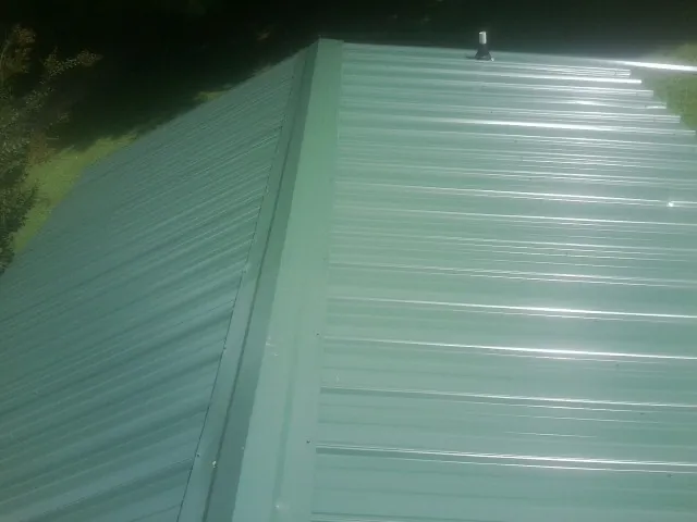 New green metal panels meeting at the ridge of a roof — Flat Roof Repair work by our crew in Cheraw
