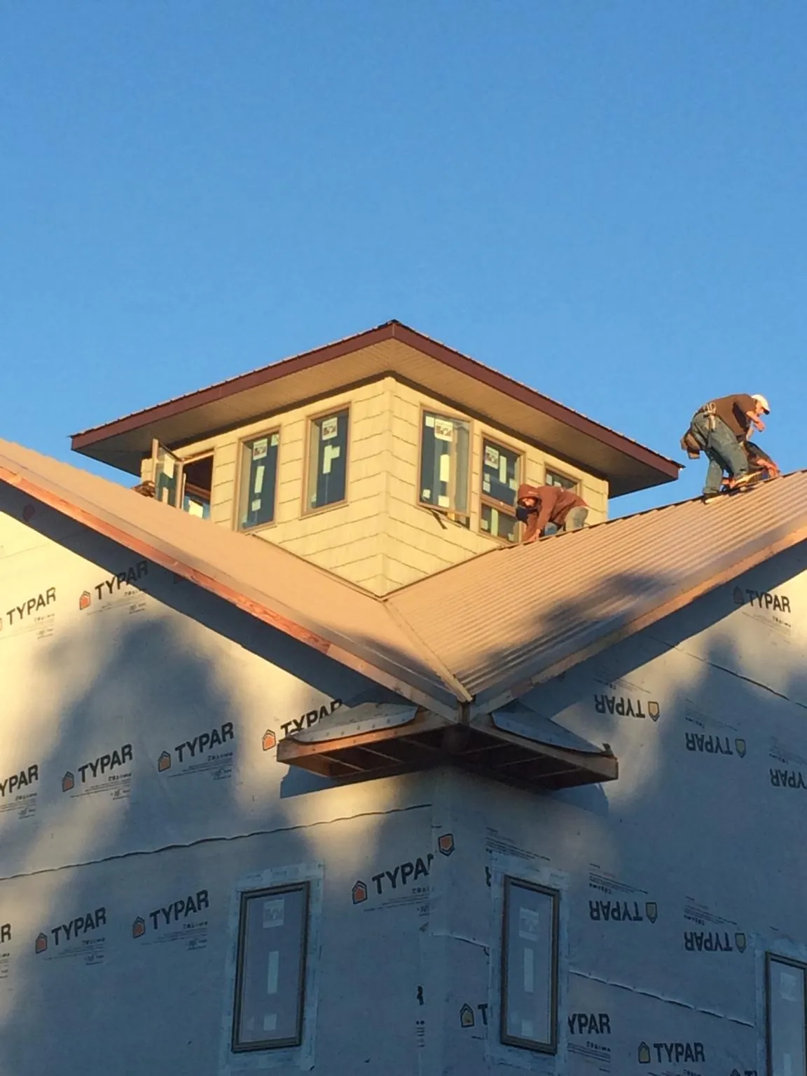 Roofers working around a rooftop cupola on a new metal roof at sunset — Roof Waterproofing in Cheraw by Roofing Brothers